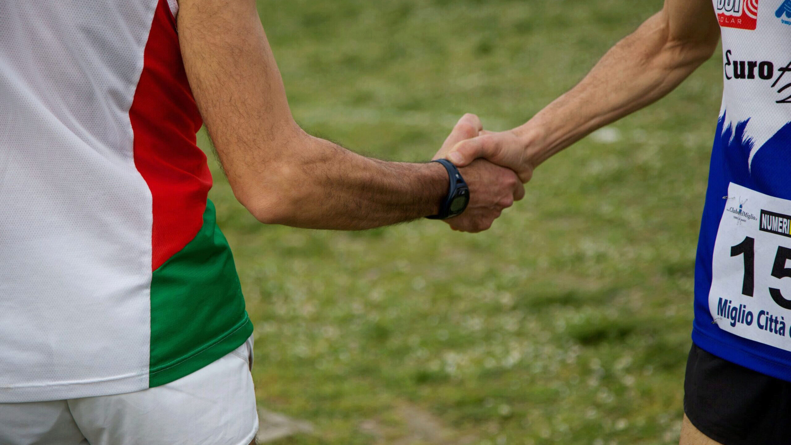 Two individuals in athletic attire are shaking hands, suggesting sportsmanship or camaraderie after a race or sports event.