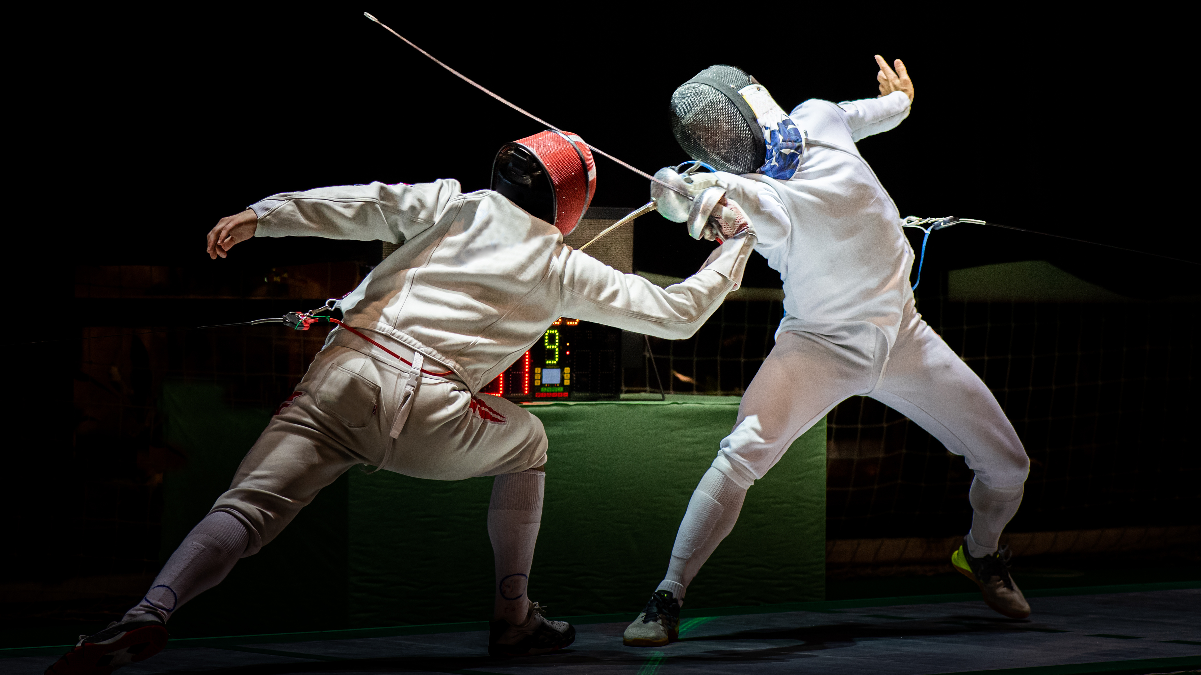 Two fencers in protective gear engage in a dynamic bout, their foils crossed. The scene captures the intensity and precision of the sport.