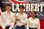 Three individuals in white shirts smile while holding a first-place trophy in front of a "Lambert High School" sign.